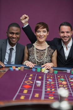 Three happy people at roulette table in casino