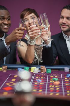 Three people toasting at roulette table in casino