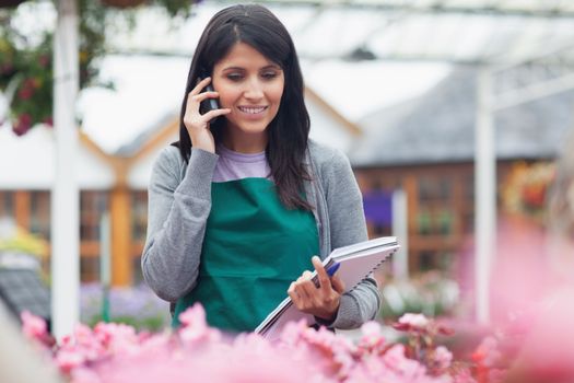 Garden center worker phoning while taking notes on flowers in center