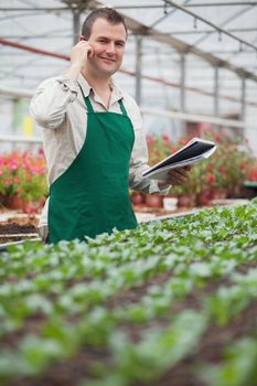 Smiling man on the phone and taking notes in greenhouse in garden center