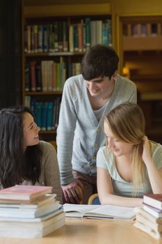 Student talking to classmates sitting at desk in college library