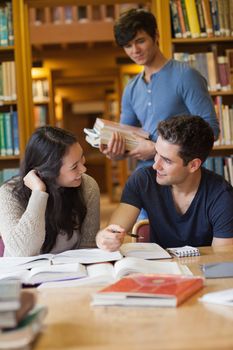 Two students studying together in college library as boy walks past holding books