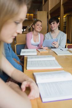 Happy students with tablet pc sitting at study table in college library