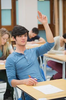 Student raising hand to ask question during exam in exam hall