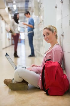 Woman sitting on the floor holding a laptop smiling in college hallway