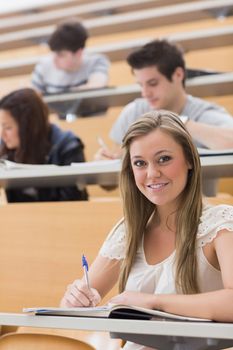 Woman sitting while smiling at the lecture hall and taking notes