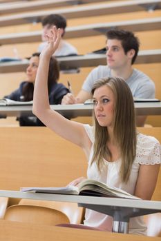 Woman sitting at the lecture hall with hand up to ask question