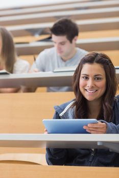 Woman holding a tablet pc while smiling and looking up in lecture hall