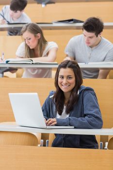 Smiling student sitting in lecture using laptop
