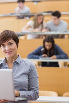 Teacher standing while holding a laptop in lecture hall