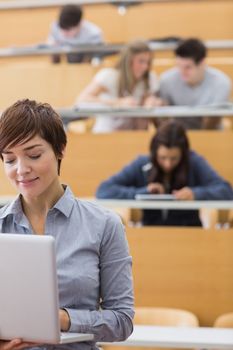 Lecturer standing while holding a laptop in lecture hall