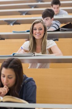 Student sitting at the lecture hall smiling and taking notes