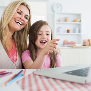 Mother and daughter laughing at laptop in the kitchen