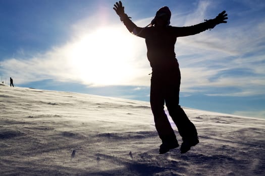 Silhouette of jumping girl on snow against the sun, concept of youth, energy, active life