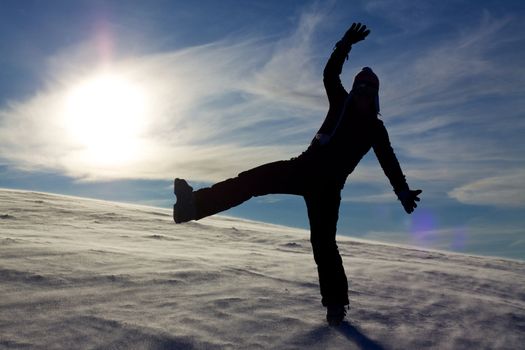 Silhouette of jumping girl on snow against the sun, concept of youth, energy, active life