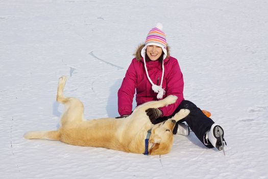Joyful attractive girl with ice skates playing with her dog on frozen lake