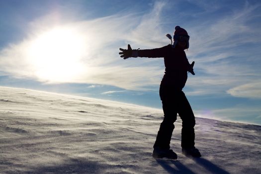 Silhouette of girl in snow spreading hands with sun in the background