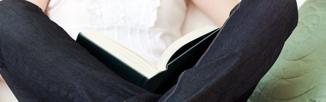 Close-up of a woman reading a book sitting on a sofa at home