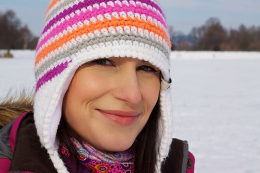 Closeup of smiling young woman wearing knitted winter cap with natural winter background