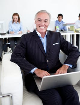 Smiling businessman using a laptop with his team in the background
