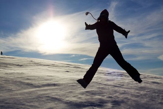 Silhouette of jumping girl on snow against the sun, concept of youth, energy, active life