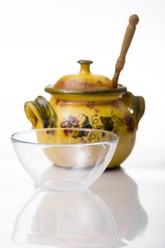 Honey jar and empty glass mug on white background