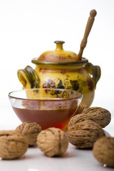 Transparent mug full of honey, honey jar and walnut on white background