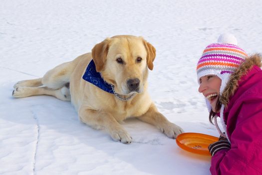 Joyful pretty girl laying with her cute dog in snow on frozen lake