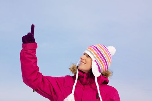 Smiling attractive girl wearing knitted winter cap and gloves pointing upwards with her finger