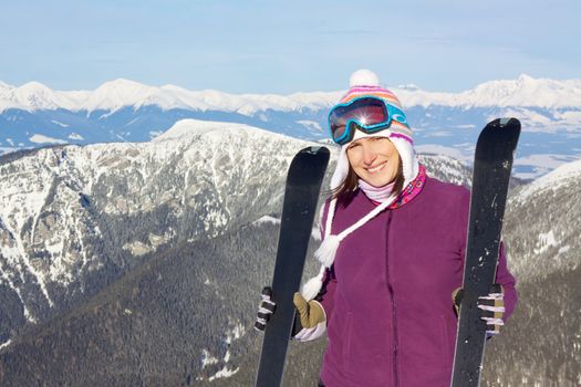 Happy attractive young girl holding skis with picturesque winter mountainous background