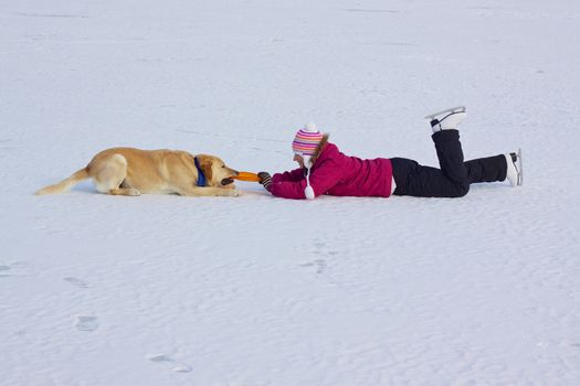 Girl with ice skates playing with her dog on frozen lake