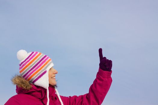 Smiling attractive girl wearing knitted winter cap and gloves pointing upwards with her finger, place for your copy