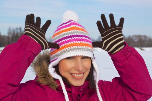 Smiling young woman wearing knitted winter cap making funny faces with natural winter background