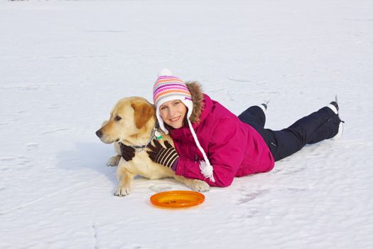 Beautiful young girl with ice skates laying with her dog in snow on frozen lake