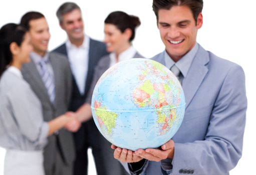 Cheerful businessman holding a globe in front of his team against a white background