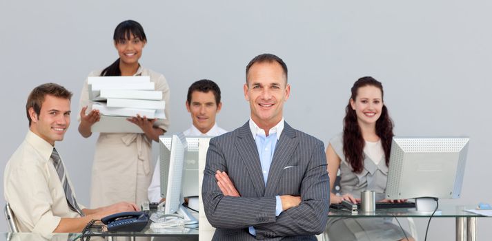 Self-assured manager with folded arms with his team in the background