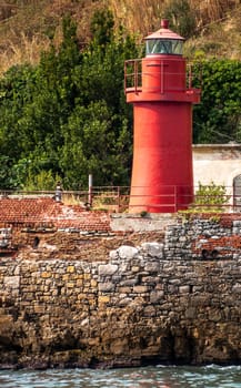 small red lighthouse on a stony shore in italy