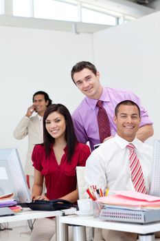 International business team smiling at the camera with their manager on phone in the background