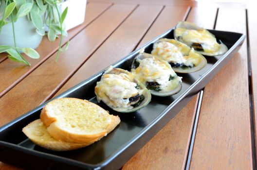 Side view of food call "Baked mussel with cheese" served on the wooden table.