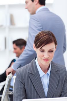 Serious businesswoman working at a computer with her colleagues in the background