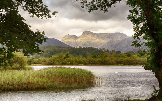 Sun rising and illuminating Langdale Pikes with Elter Water in foreground