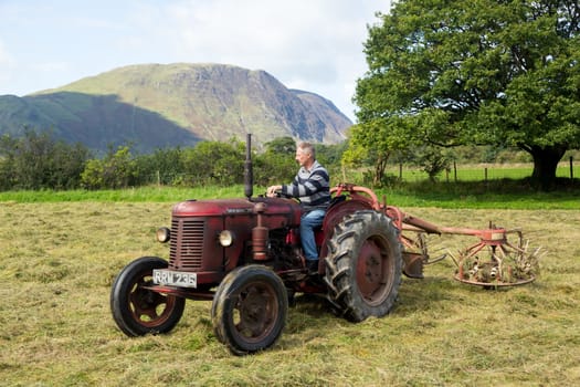 BUTTERMERE, ENGLAND - SEPTEMBER 5: Farmer threshing corn using antique tractor on September 5, 2012.