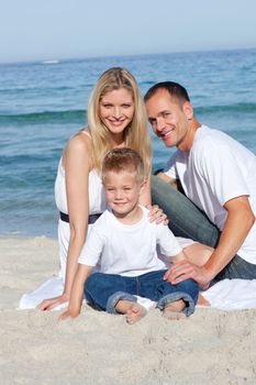 Portrait of cheerful parents with their son sitting on the sand at the beach