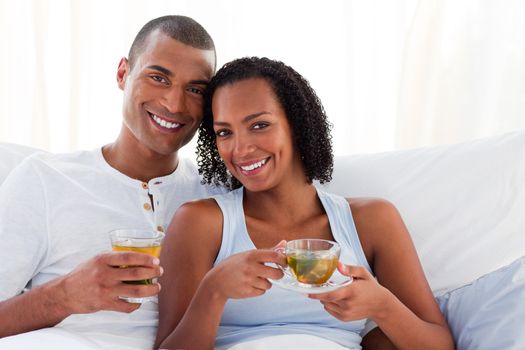 Smiling couple drinking a cup of tea on their bed. Concept of love.