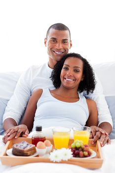 Afro-american couple having breakfast lying on their bed. Concept of love.