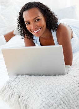 Cheerful young woman using a laptop lying on her bed