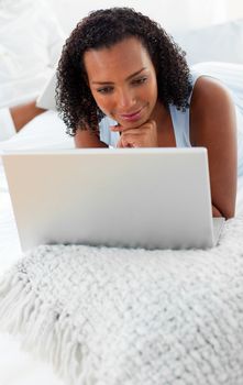 Smiling young woman using a laptop lying on her bed