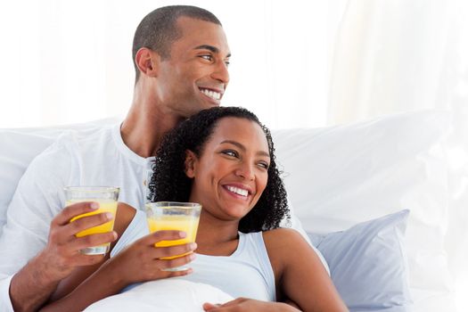 Romantic couple drinking orange juice lying on their bed