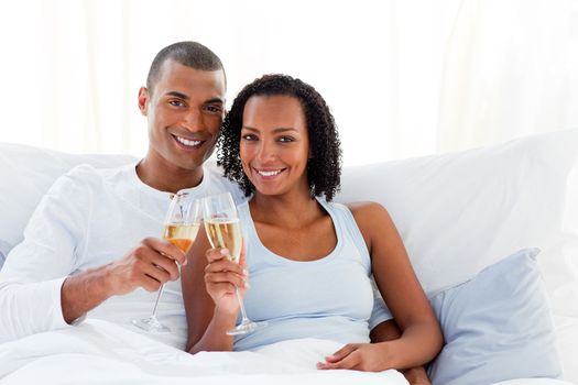 Romantic couple toasting with Champagne lying on their bed