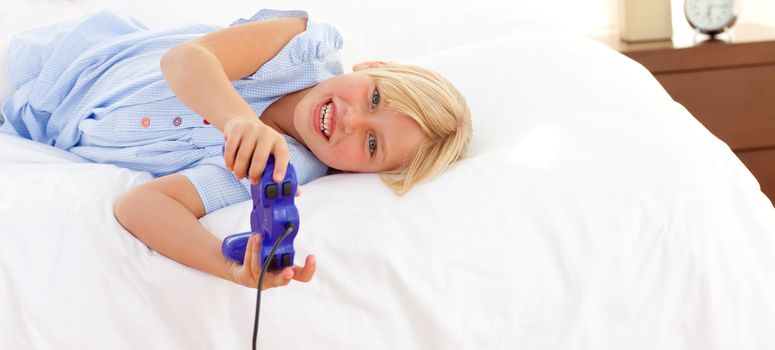 Adorable little girl playing video game lying on bed